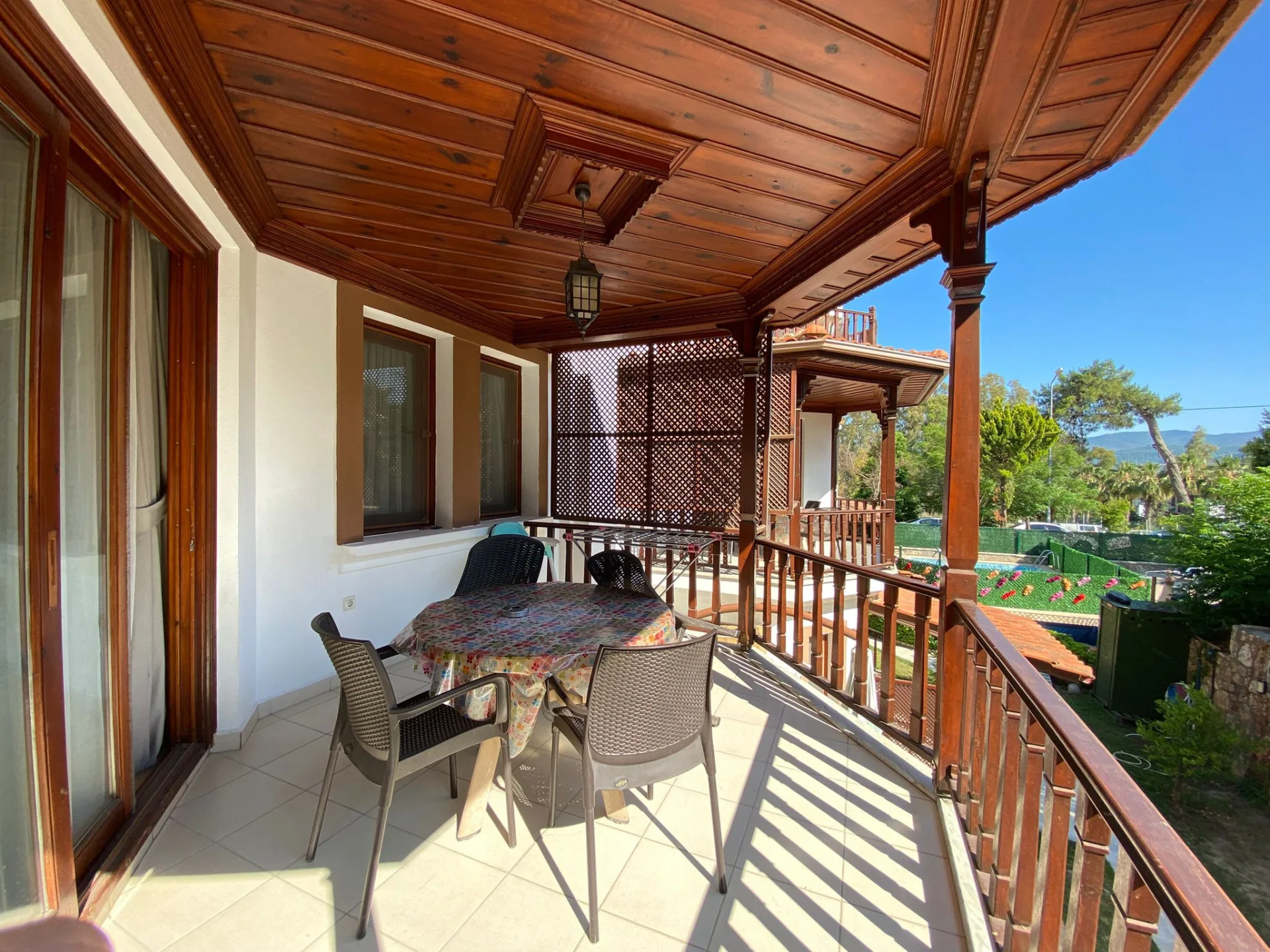 1+1 daire balkon; ahşap veranda, oturma masası ve tesis çevresi manzarası